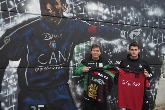 Elías y Migue Tomé sujetan las camisetas de sus equipos junto al mural de Juan Carlos Unzué en el campo del Orcoyen.