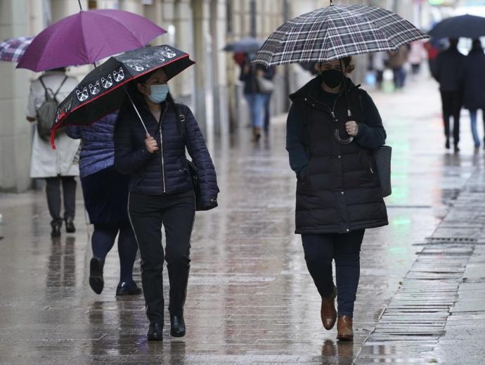 Personas andando por la calle con paraguas para protegerse de la lluvia y mascarilla para evitar contagios de coronavirus