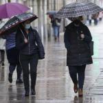 Personas andando por la calle con paraguas para protegerse de la lluvia y mascarilla para evitar contagios de coronavirus