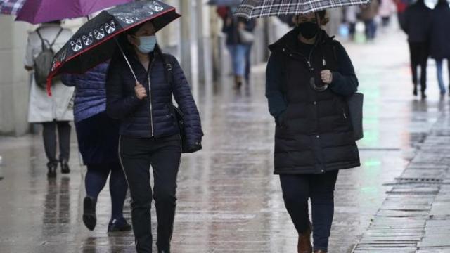 Personas andando por la calle con paraguas para protegerse de la lluvia y mascarilla para evitar contagios de coronavirus