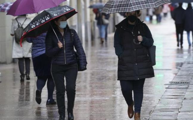 Personas andando por la calle con paraguas para protegerse de la lluvia y mascarilla para evitar contagios de coronavirus