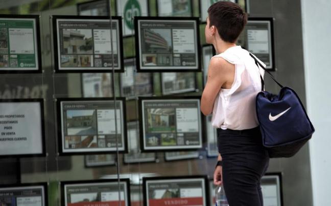 Una joven, ante el escaparate de una inmobiliaria con ofertas de pisos en venta y alquiler.