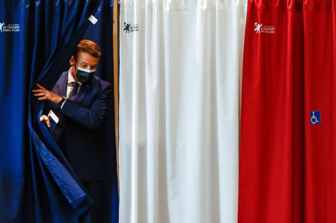 Macron, saliendo de la cabina, con los colores de la bandera francesa, con su papeleta para votar en las elecciones regionales.