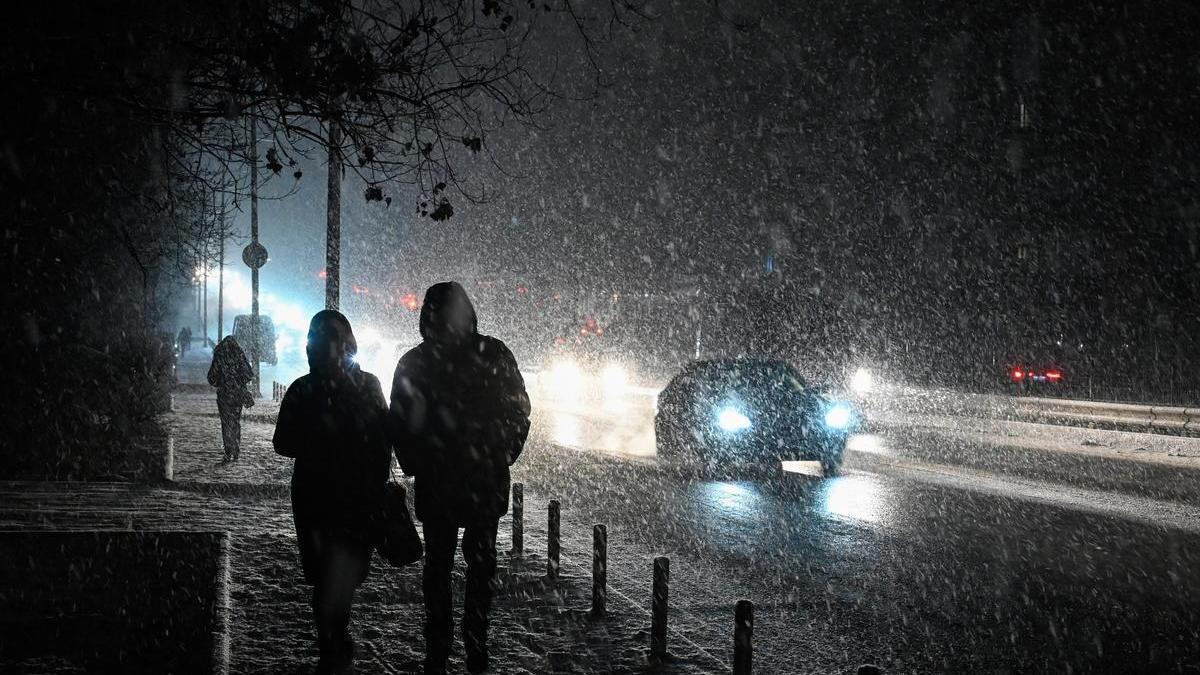 Varias personas pasean por una calle a oscuras de Kiev en plena tormenta de nieve.