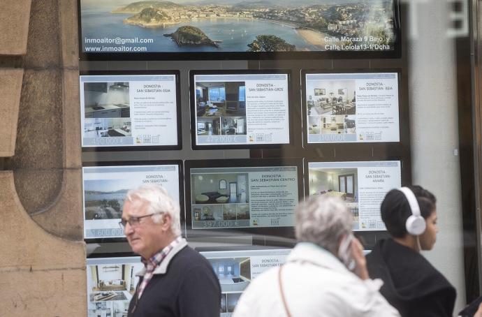 Personas pasan frente a una inmobiliaria en Donostia.