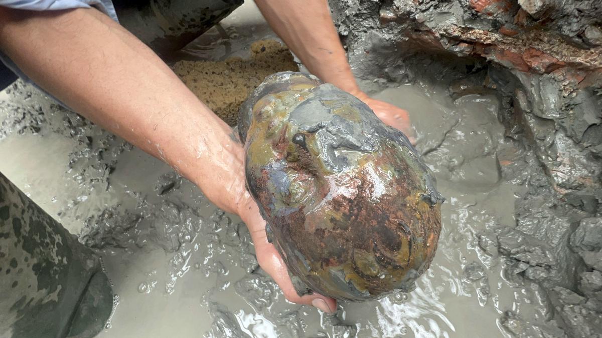 Un arqueólogo saca del barro la estatua de la cabeza de un niño-