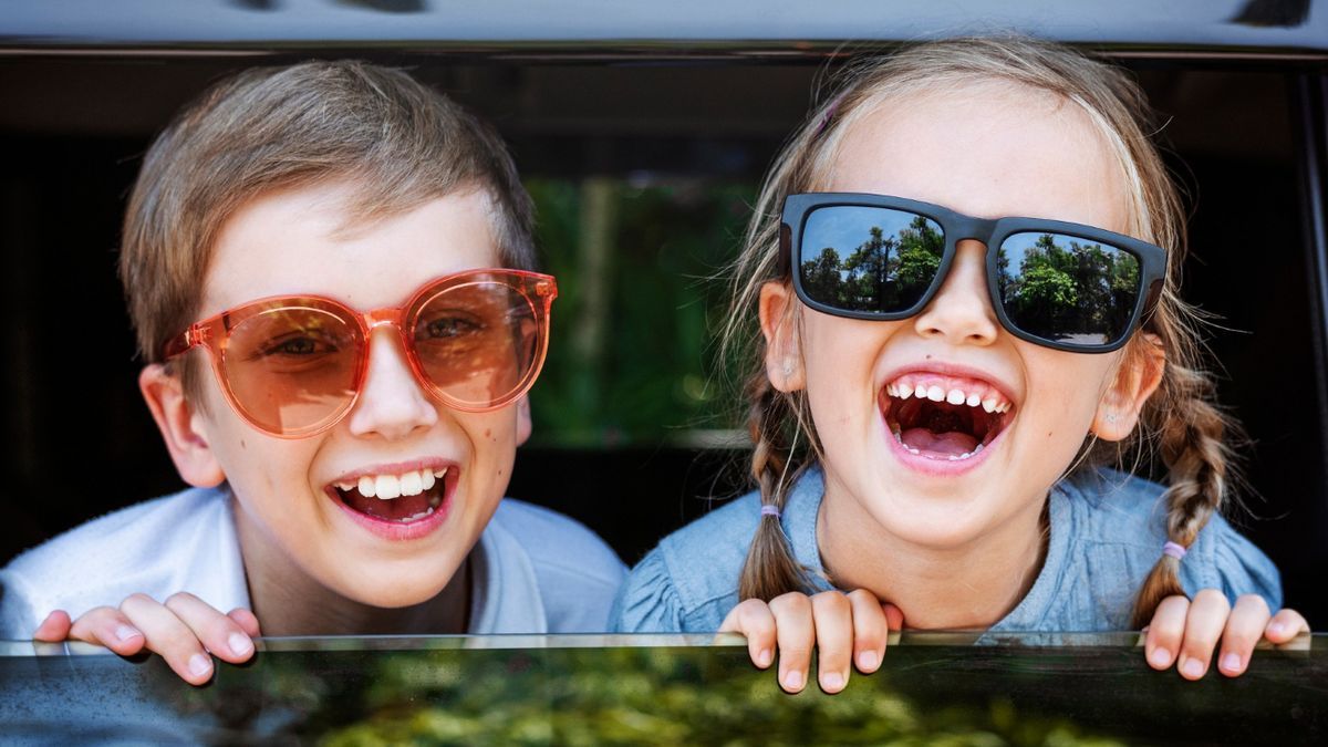 Una pareja de niños sonríe desde la ventanilla del coche, rumbo a su destino vacacional.