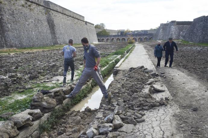 Personas paseando por los fosos de la Ciudadela mientras los trabajadores reparan los destrozos ocasionados una vez retirada la arena y el mobiliario que se utilizó para el concurso de hípica.