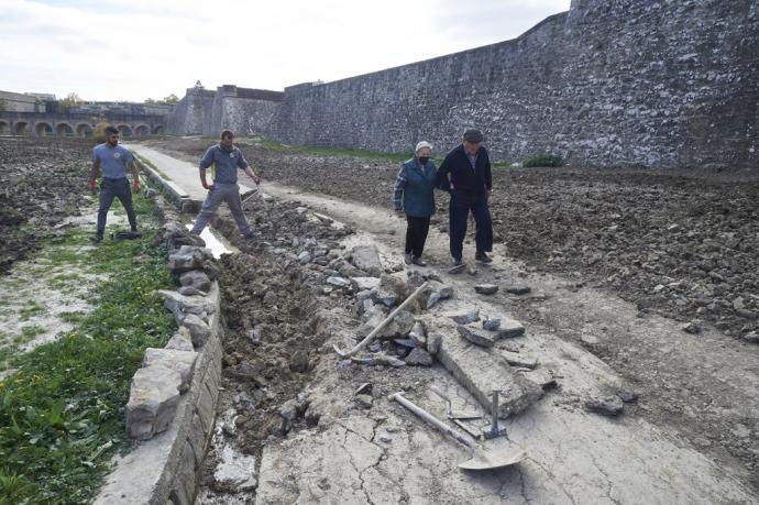 Personas paseando por los fosos de la Ciudadela mientras los trabajadores reparan los destrozos.