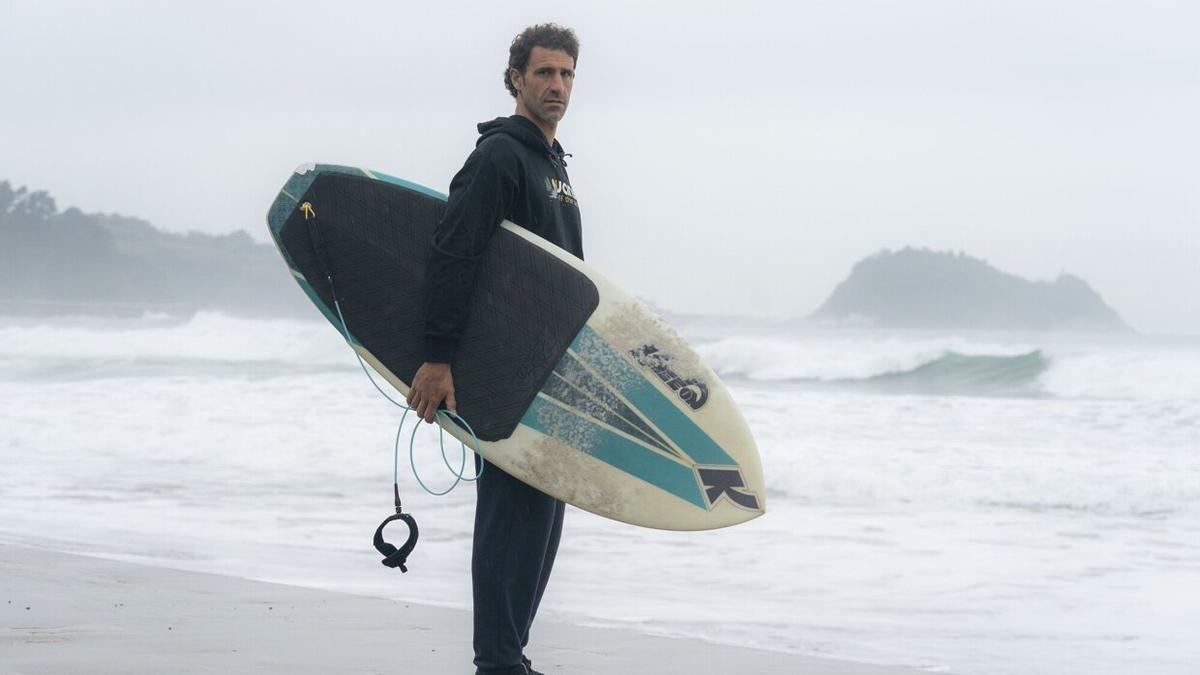 Ibon Oregi posa con una tabla de surf en la playa de Zaratuz, al fondo el ratón de Getaria.