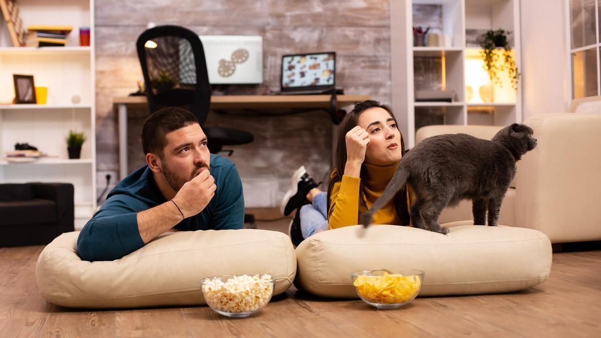 Una pareja come patatas y palomitas mientras ve la tele.