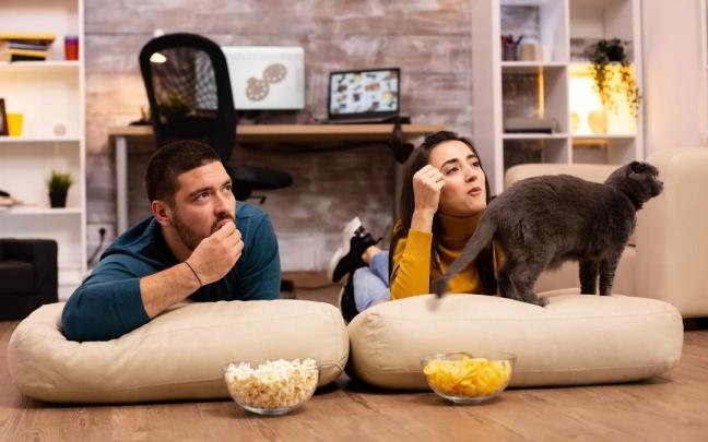 Una pareja come patatas y palomitas mientras ve la tele. Una pareja come patatas y palomitas mientras ve la tele.