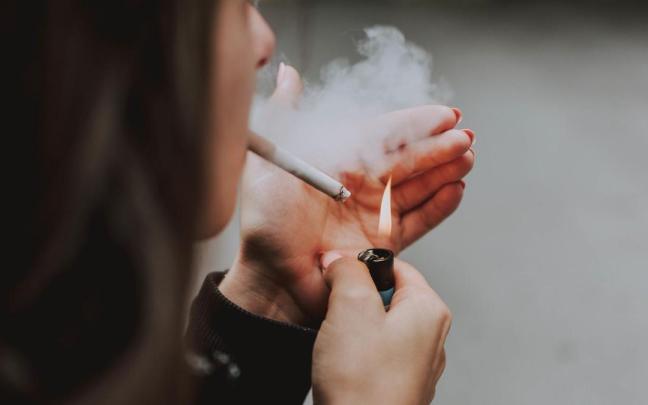 Una mujer enciende un cigarrillo con un mechero. Una mujer enciende un cigarrillo con un mechero.