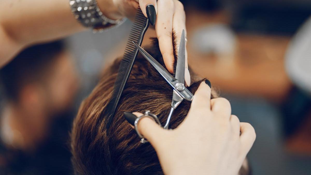Una mujer corta el pelo a un hombre en una peluquería.