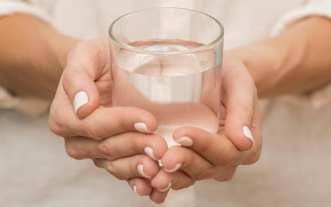 Una mujer sujeta un vaso de agua en sus manos.