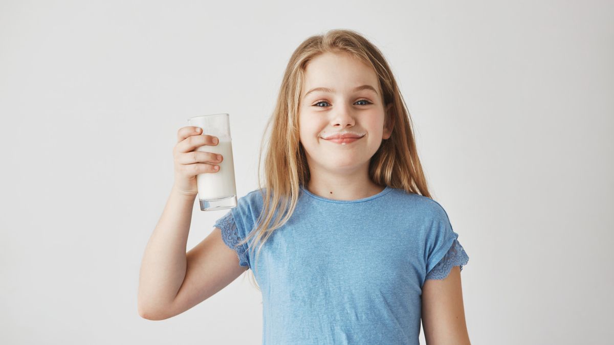 Niña sujetando un vaso de leche.