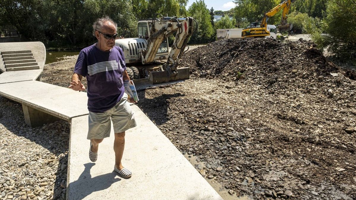 Un hombre cruza la pasarela del río Arga con maquinaria trabajando detrás.