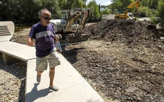Un hombre cruza la pasarela del río Arga con maquinaria trabajando detrás. Un hombre cruza la pasarela del río Arga con maquinaria trabajando detrás.