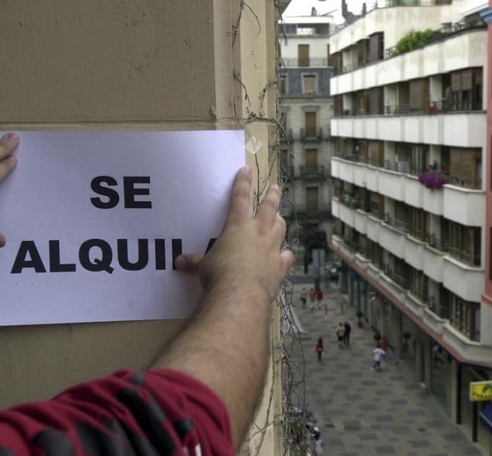 Un hombre instala un cartel que anuncia el alquiler de una vivienda.