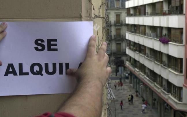 Un hombre instala un cartel que anuncia el alquiler de una vivienda.