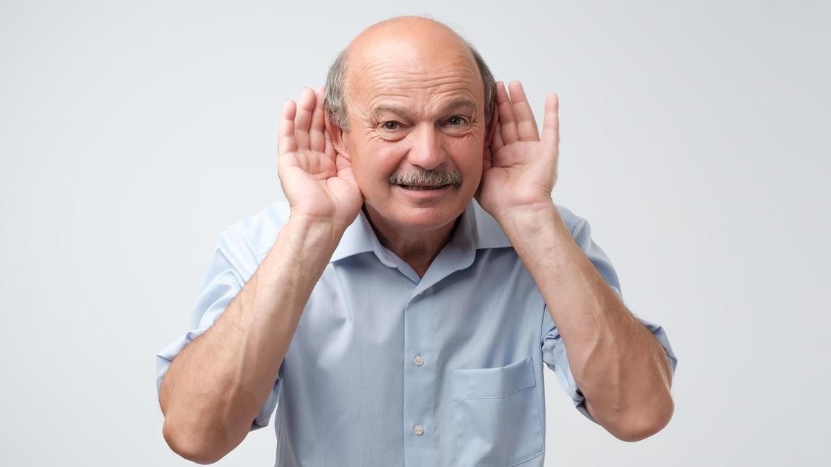 Un hombre mayor hace el gesto de no oír bien.