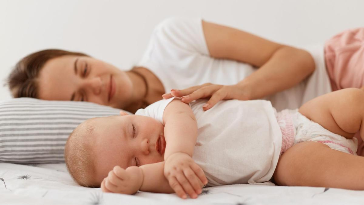 Una mujer acostada en la cama junto a su bebé dormido.