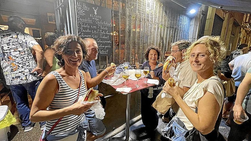 Un grupo de personas disfrutan sonrientes de los bocadillos en la puerta de un bar.