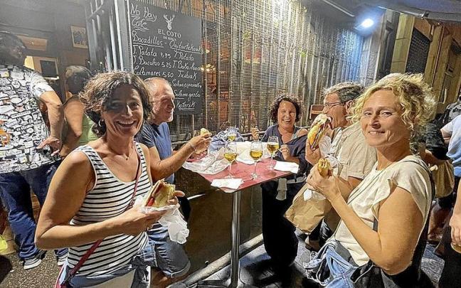 Un grupo de personas disfrutan sonrientes de los bocadillos en la puerta de un bar.