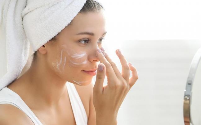 Una mujer se aplica crema hidratante en el rostro.