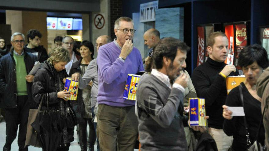 Cinéfilos hacen cola para entrar en el cine con sus palomitas en la mano.