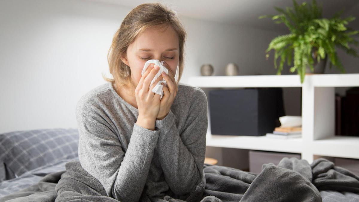 Una mujer aquejada de gripe se suena la nariz.