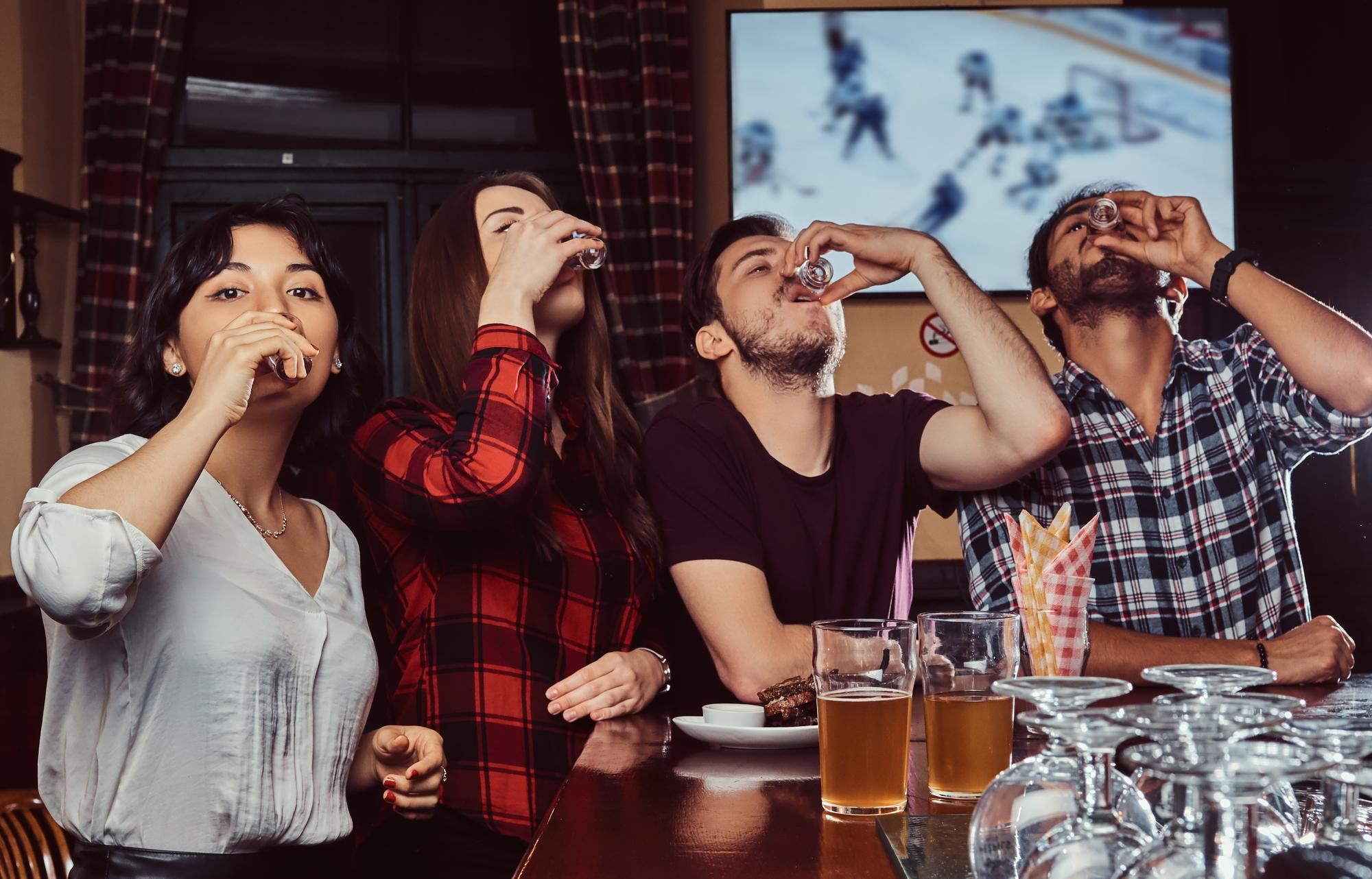 Cuatro jóvenes beben chupitos en la barra de un bar.