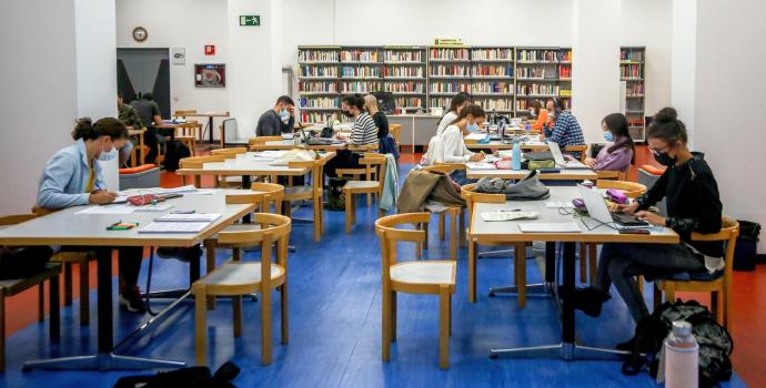 Varias personas estudian en una biblioteca con la mascarilla puesta.