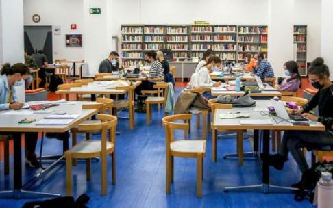 Varias personas estudian en una biblioteca con la mascarilla puesta.