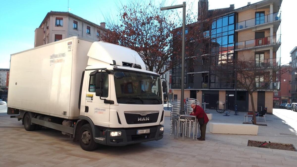 Un cliente del Mochuelo, con su vino y la prensa en una mesa de la terraza sin montar. El camión pasa a su lado por la zona peatonal.