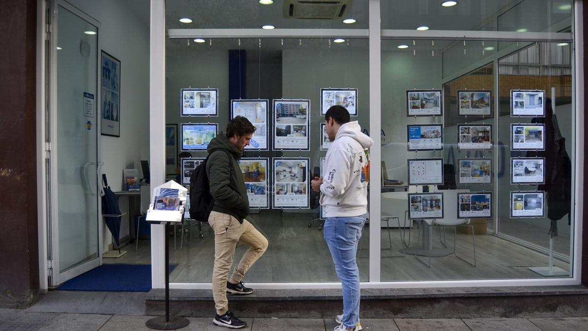Dos jóvenes miran precios en una inmobiliaria.