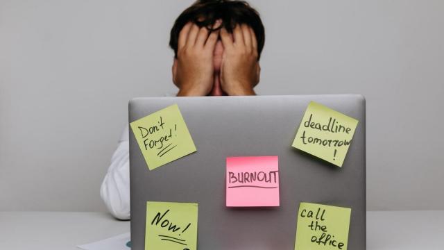 Un hombre agotado tras un port&aacute;til lleno de poss-it en uno de los cuales se lee 'burnout'.