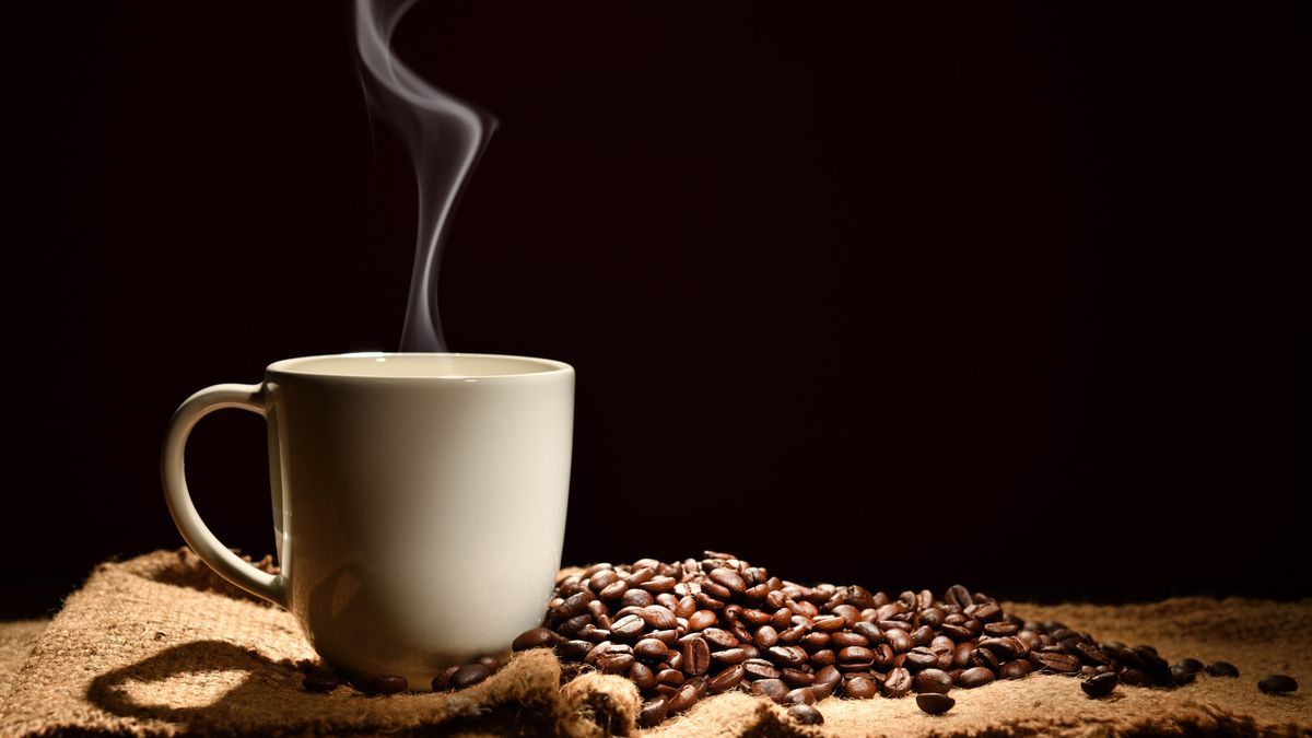 Taza humeante con granos de café al lado.