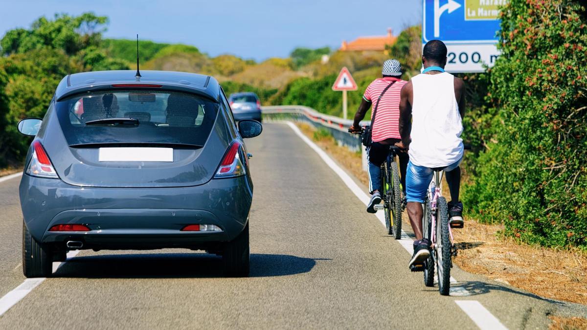Un coche adelanta a dos ciclistas en una carretera.