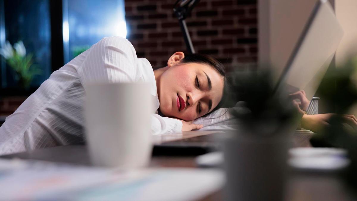 Una mujer se queda dormida apoyada en su mesa de trabajo.