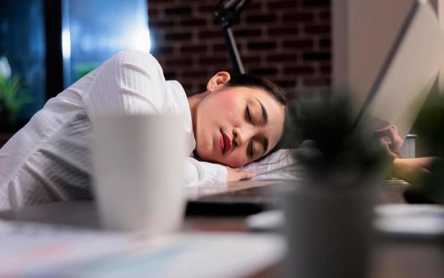 Una mujer se queda dormida apoyada en su mesa de trabajo.