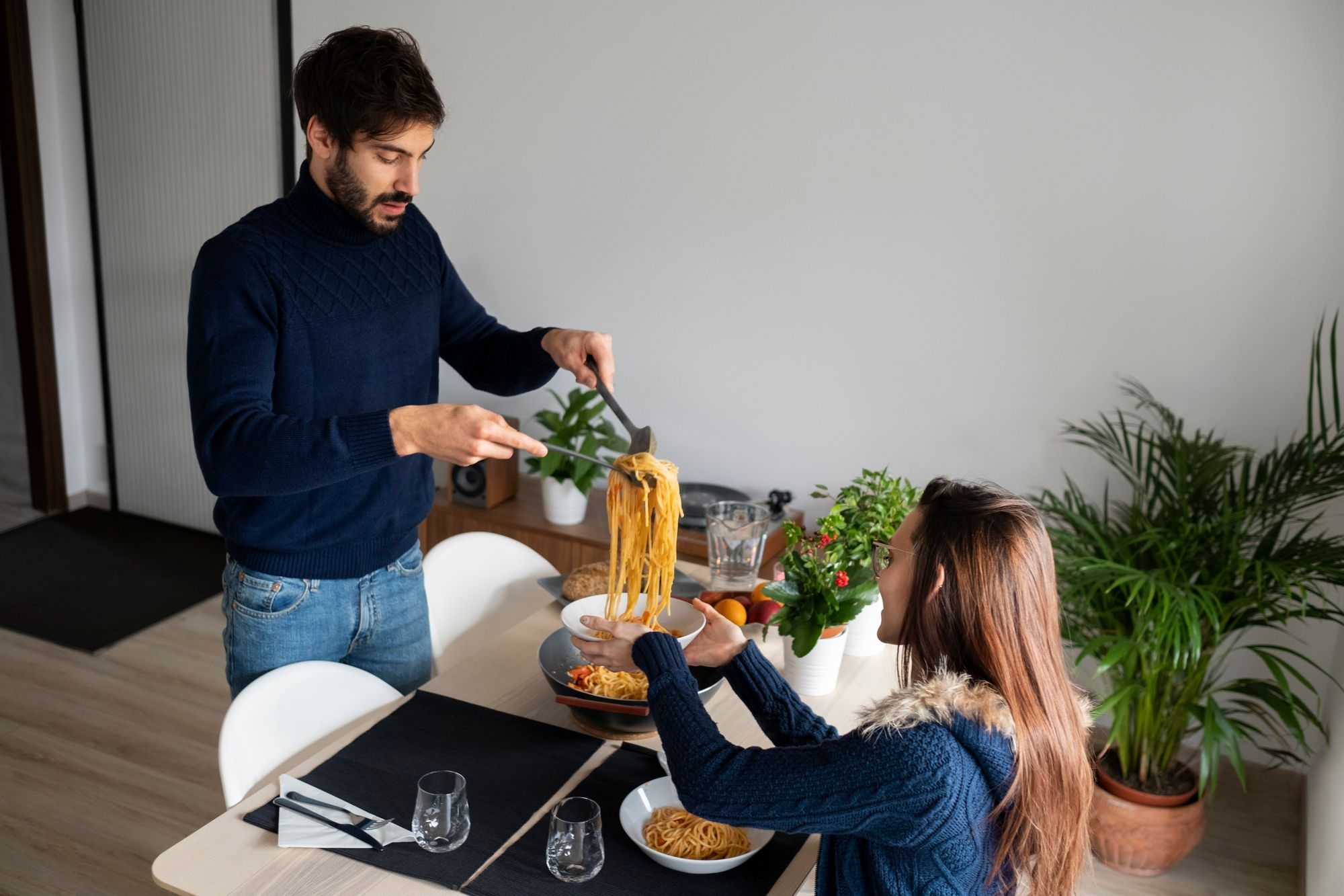 Un hombre sirve un plato de pasta a su pareja.
