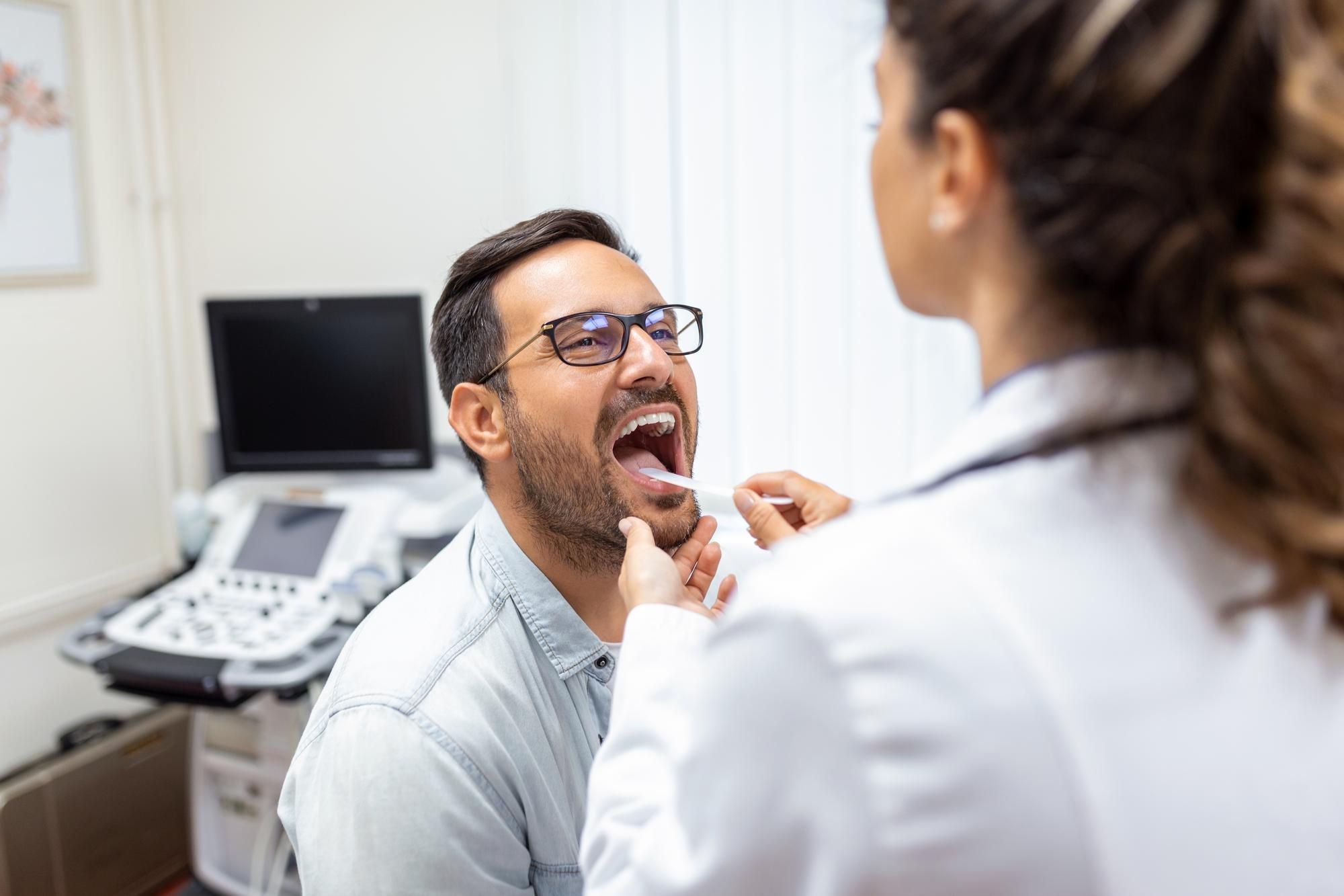 Una médico explora la garganta de un paciente.