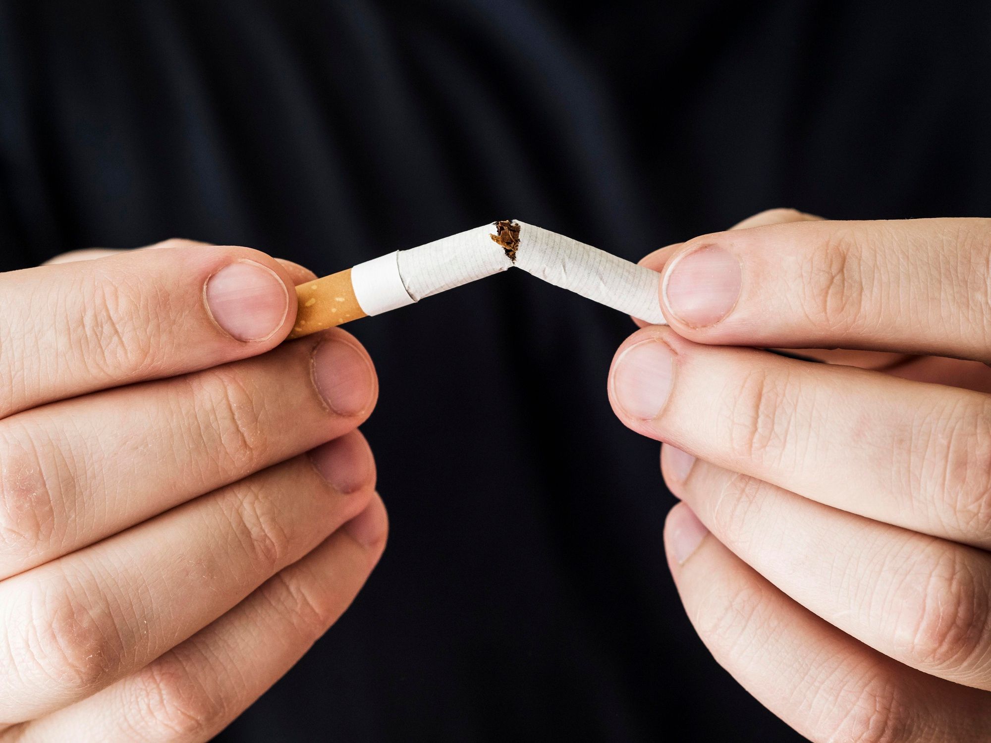 Un hombre rompe por la mitad un cigarrillo.