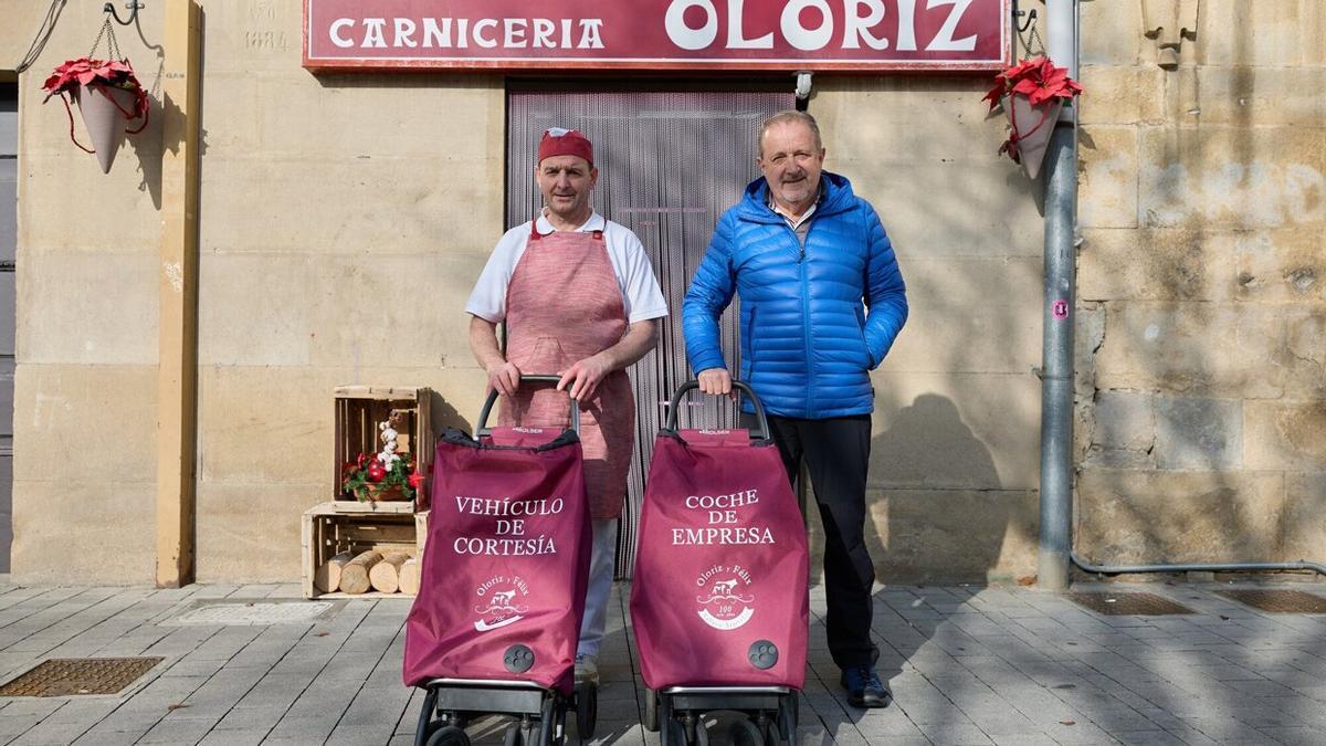 Félix Ilarraz y Juan José Olóriz posan en el exterior de la carnicería con los ‘vehículos motorizados’ con los que realizan los pedidos a domicilio.