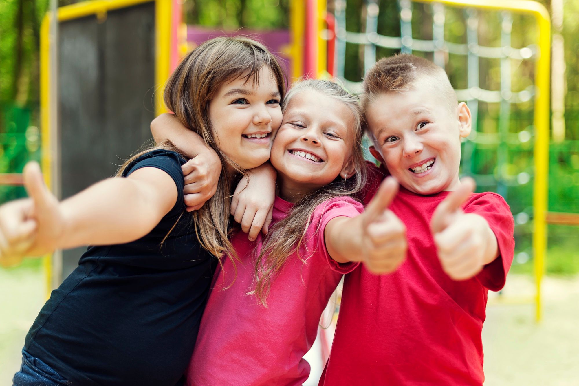 Dos niñas y un niño posan sonrientes con el pulgar hacia arriba.