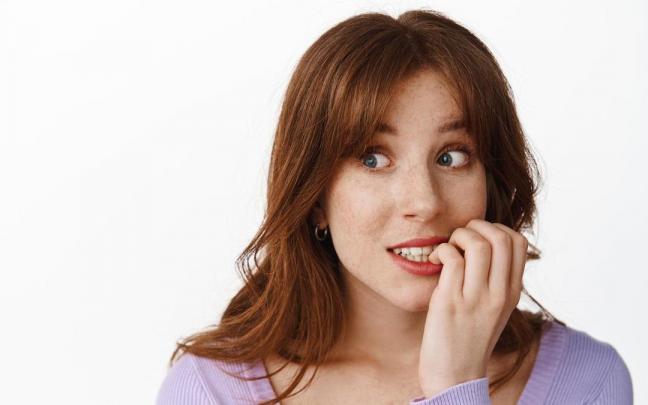 Una mujer se muerde la uña del dedo meñique.