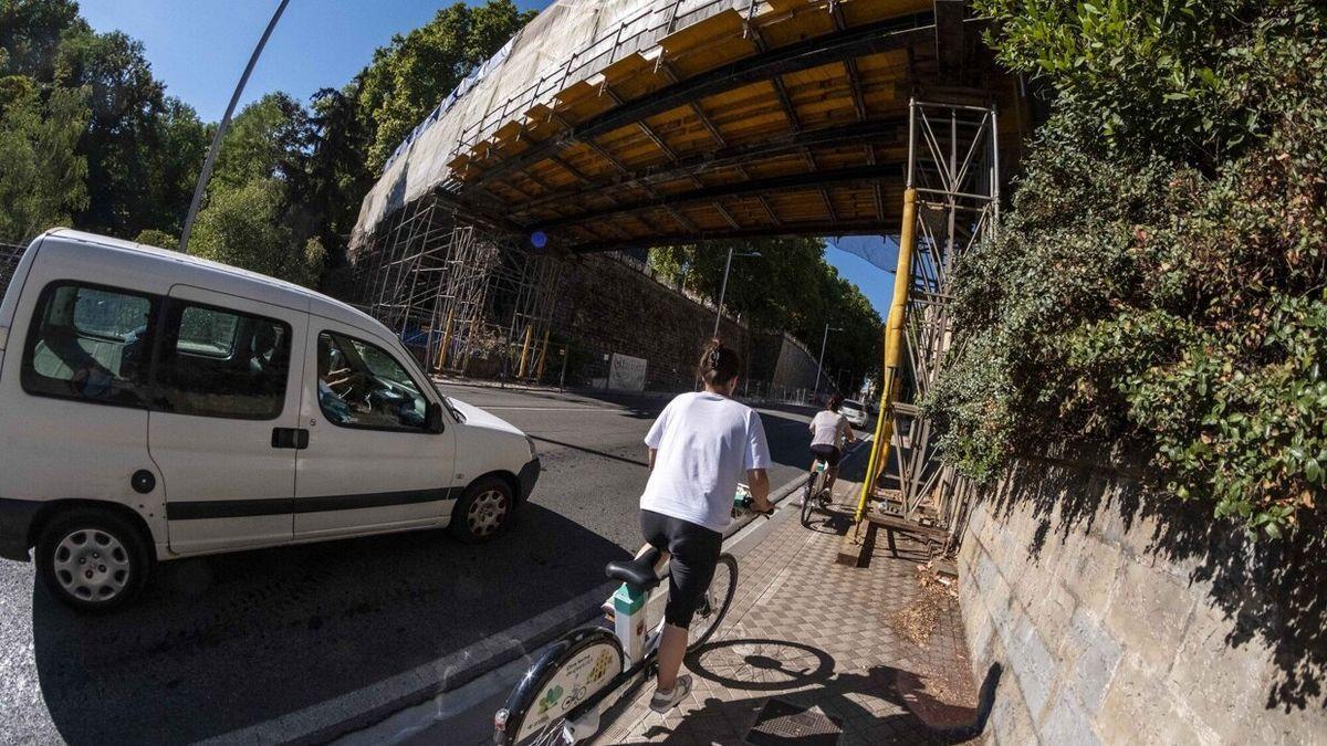 Una ciclista circula por el carril en la acera en la cuesta del Labrit bajo los andamios de la pasarela.