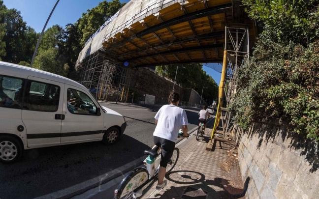 Una ciclista circula por el carril en la acera en la cuesta del Labrit bajo los andamios de la pasarela.