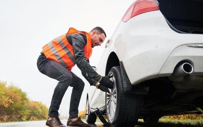 Hombre cambia la rueda de su con la ayuda de un gato.